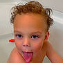 child, toddler, bathtub, bath, curly_hair, tongue_out, blue_eyes, skin, water_drops, playful, bathroom, toy, white_tiles, sitting, naked, cute, fun, expression, indoors, young