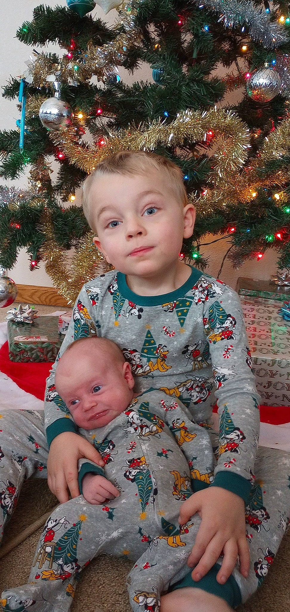 Evan is registered to the contest to win money with this photo: baby_toddler_clothing, cheek, christmas_ornament, christmas_tree, eye, face, facial_expression, green, hair, hairstyle, happy, head, human, human_body, iris, person, photograph, skin, sleeve, standing