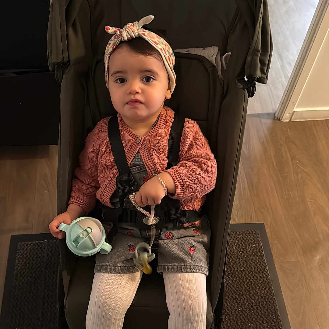 Mariame a rejoint le concours — aidez-le/la à gagner de superbes lots ! baby, bracelet, carpet, casual_clothing, child, curly_hair, cute, headband, indoor, pacifier, person, pink_cardigan, pink_shoes, seated, sippy_cup, stroller, toddler, white_tights, wooden_floor, young_child