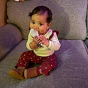 Freya joined the competition — help win amazing prizes! baby, child, toddler, sitting, couch, sofa, snack, eating, smiling, portrait, indoors, home, furniture, clothing, sweater, pants, boots, floral_pattern, dark_hair, happy