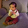 baby, child, toddler, sitting, couch, sofa, snack, eating, smiling, portrait, indoors, home, furniture, clothing, sweater, pants, boots, floral_pattern, dark_hair, happy