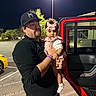 Freya is registered to the contest to win money with this photo: baby, child, adult, father, parent, portrait, night, outdoor, parking_lot, jeep, vehicle, red_car, bow, dress, socks, holding, family, face, streetlight, smiling