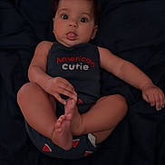 Freya is registered to the contest to win money with this photo: baby, baby_pose, blanket, child, clothing, cute, dark_background, expression, face, foot, hand, indoors, infant, lying_down, onesie, person, portrait, skin, tongue_out, young_child