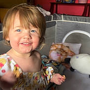 Ivy is registered to the contest to win money with this photo: toddler, child, smiling, indoor, playpen, blanket, toy, furniture, room, blue_eyes, happy, face, person, plush, cushion, clothing, head, hair, home, baby