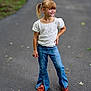 child, girl, standing, jeans, flared_jeans, brown_shoes, ponytail, blonde_hair, white_top, floral_pattern, outdoor, paved_path, casual_clothing, smile, confident, fashion, young, nature, leaf, playful