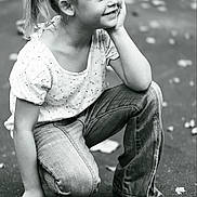 Mariah is registered to the contest to win money with this photo: child, girl, smiling, crouching, jeans, white_shirt, pony_tail, outdoor, pavement, leaves, casual_clothing, happy, portrait, young, nature, playful, daylight, monochrome, black_and_white, person