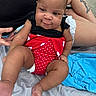 Kailani joined the competition — help win amazing prizes! baby, infant, polka_dot, swimsuit, red, black, blanket, blue_towel, tattoo, leg, hand, skin, outdoor, sitting, cute, chubby, person, clothing, foot, portrait