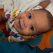 Kailani is registered to the contest to win money with this photo: baby, child, smiling, face, eyes, colorful_clothing, onesie, indoor, blanket, playmat, happy, infant, person, cute, portrait, head, skin, cheerful, expression, young