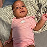 baby, infant, pink_onesie, nike_logo, blanket, bed, bedding, soft_lighting, skin, face, eyes, hand, arm, legs, person, indoors, portrait, cute, comfortable, expression