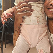 Ciara is registered to the contest to win money with this photo: baby, bow, casual, chair, child, curious, cute, earrings, floral_outfit, holding_hands, indoor, menu, person, pink_shoes, portrait, smiling_adult, sneakers, table, tattoo, wooden_walls