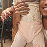 Ciara is registered to the contest to win money with this photo: baby, child, pink_shoes, floral_outfit, smiling_adult, indoor, wooden_walls, curious, holding_hands, person, tattoo, earrings, bow, sneakers, table, menu, chair, casual, portrait, cute