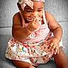 baby, child, clothing, cute, face, floral, foot, hand, headband, headwear, indoors, infant, person, playful, portrait, sitting, skin, skirt, smiling, soft_surface