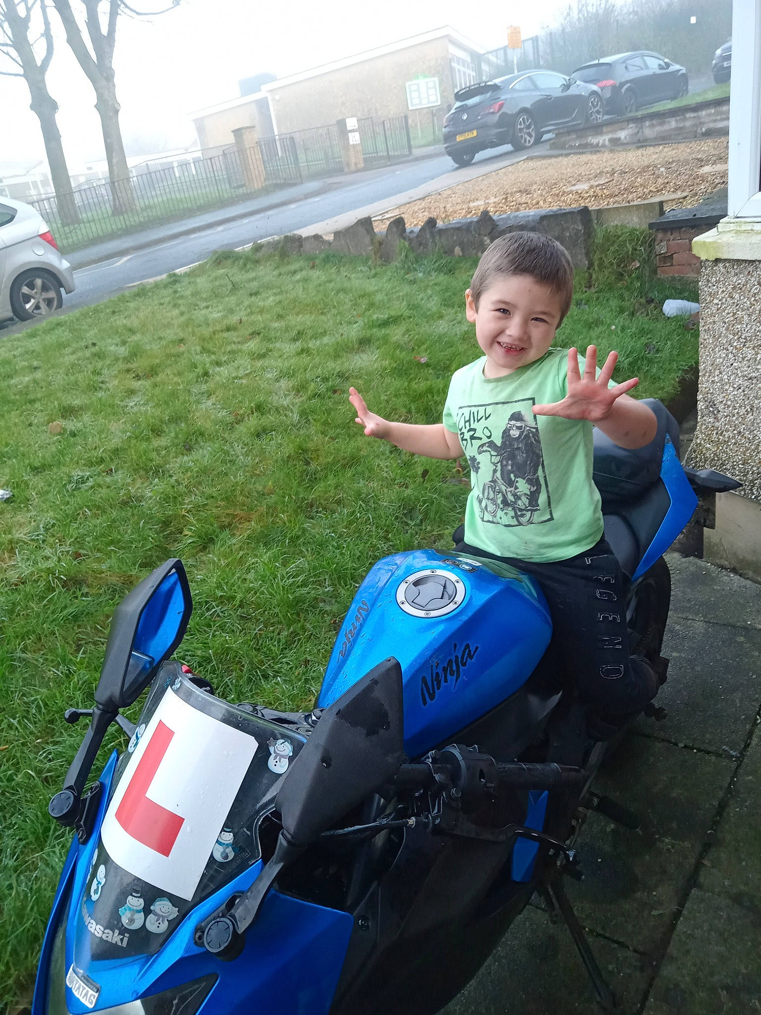 Theo is registered to the contest to win money with this photo: asphalt, automotive_design, automotive_exterior, automotive_tire, fender, fun, grass, joy, land_vehicle, leisure, motor_vehicle, person, plant, rim, shorts, smile, spoke, tire, toddler, tree