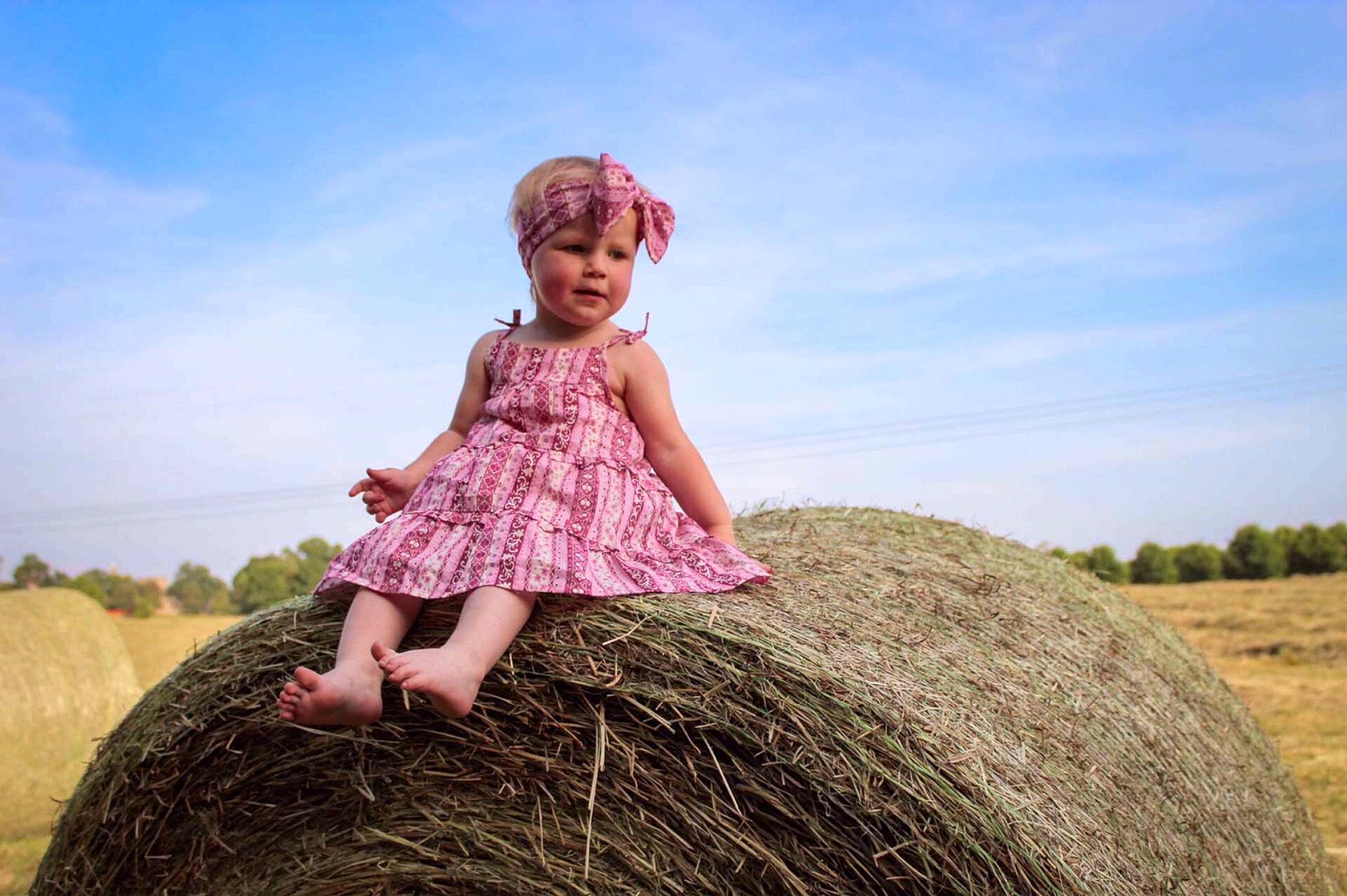 Heather is registered to the contest to win money with this photo: agriculture, baby_toddler_clothing, cloud, flash_photography, fun, grass, grassland, happy, hat, headwear, landscape, magenta, people_in_nature, person, prairie, sitting, sky, smile, soil, sun_hat