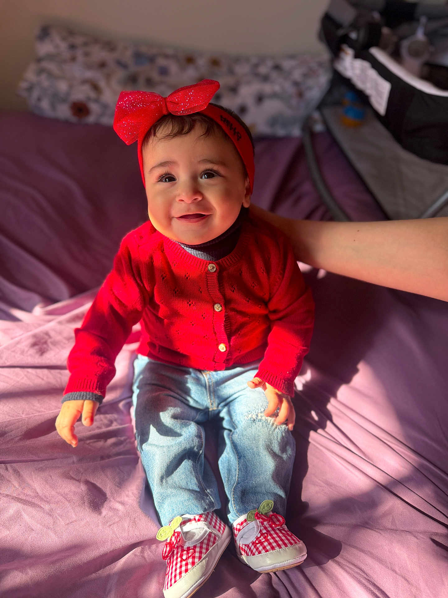 Zainab Samhan joined the competition — help win amazing prizes! baby, child, smiling, red_sweater, headband, jeans, shoes, indoor, bed, hand, person, happy, cute, portrait, sitting, sunlight, clothing, footwear, infant, casual