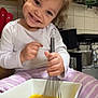 child, toddler, kitchen, whisk, bowl, eggs, cooking, smile, happy, curly_hair, white_shirt, striped_pants, floor, tile, home, person, playful, cute, activity, indoors