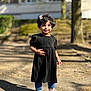 child, smiling, outdoor, dress, black_dress, blue_leggings, pink_sneakers, curly_hair, hair_accessory, sunny, daylight, shadow, sidewalk, nature, tree, person, cute, happy, portrait, young