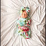 newborn, baby, swaddled, blanket, bow, headband, floral_pattern, sleeping, white_sheet, bed, cozy, infant, cute, resting, portrait, soft_lighting, wrapped, peaceful, child, indoors
