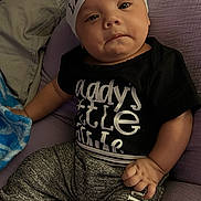 Stephen joined the competition — help win amazing prizes! baby, child, infant, hat, clothing, blanket, cushion, purple, black_shirt, pants, striped_cuffs, text_on_clothes, face, hand, indoor, portrait, cute, small_person, relaxed, seated