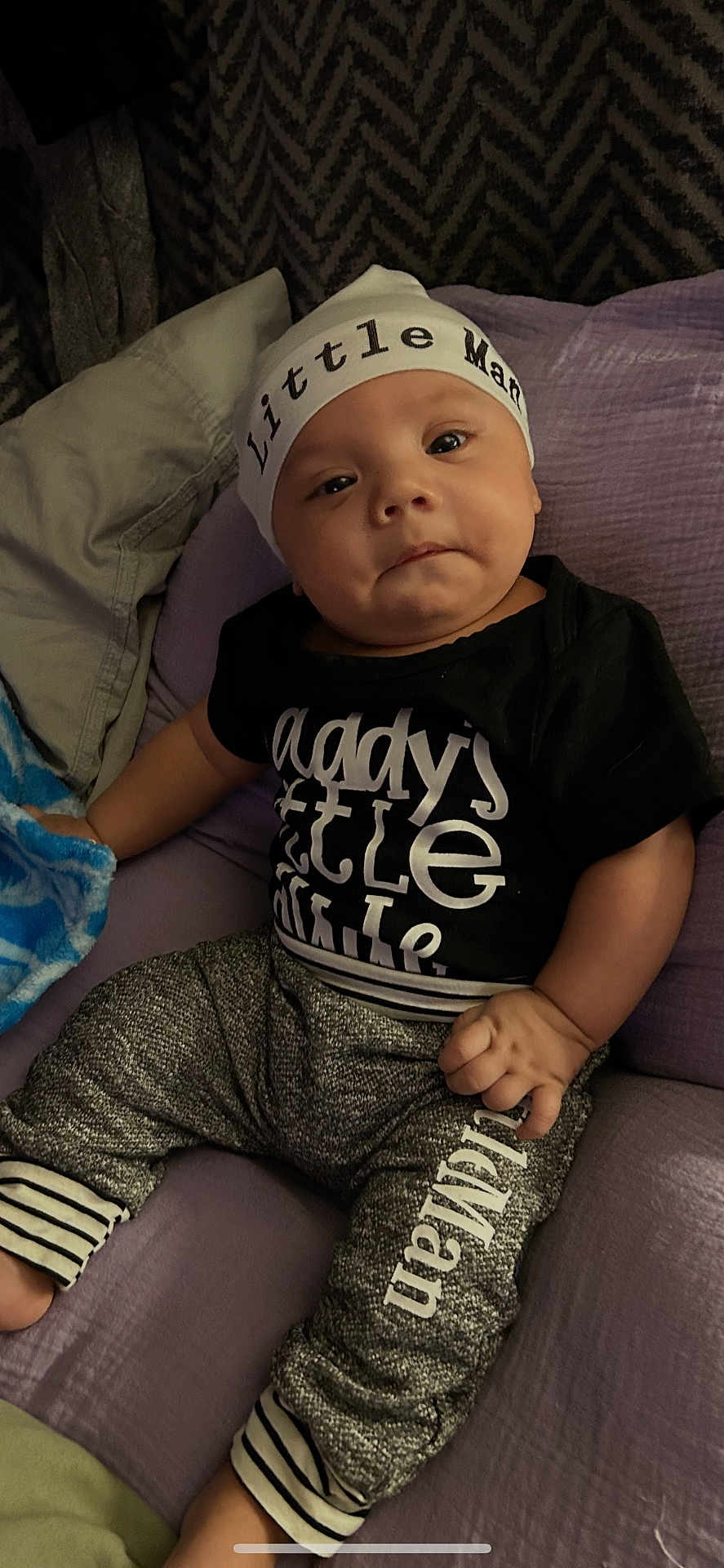 Stephen joined the competition — help win amazing prizes! baby, child, infant, hat, clothing, blanket, cushion, purple, black_shirt, pants, striped_cuffs, text_on_clothes, face, hand, indoor, portrait, cute, small_person, relaxed, seated