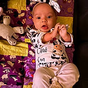 Cheyenne joined the competition — help win amazing prizes! baby, infant, child, cow_print, headband, bow, quilt, patchwork, toy, stuffed_animal, clothing, lying_down, cute, playful, indoor, person, face, hands, smiling, fabric