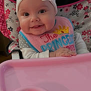 Cheyenne is registered to the contest to win money with this photo: baby, baby_accessory, bib, black, child, clothing, cute, face, happy, headband, high_chair, indoor, infant, person, pink, portrait, seat, smile, toy, white