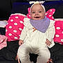 baby, smiling, infant, headband, bib, white_clothing, pink_bows, socks, polka_dot_pillow, pink_pillow, black_bed, love_sign, indoor, child, cute, happy, portrait, seated, plush_blanket, cozy