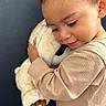 child, teddy_bear, hug, smile, cuddly_toy, soft_toy, curly_hair, beige_clothing, portrait, closeup, tender_moment, cute, indoor, warmth, affection, baby, person, happy, love, cozy