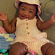 Aniya joined the competition — help win amazing prizes! baby, child, smiling, hat, striped_clothing, sitting, blanket, couch, happy, cute, indoor, person, infant, plush, relaxing, portrait, arms_up, buttoned_outfit, skin, headwear