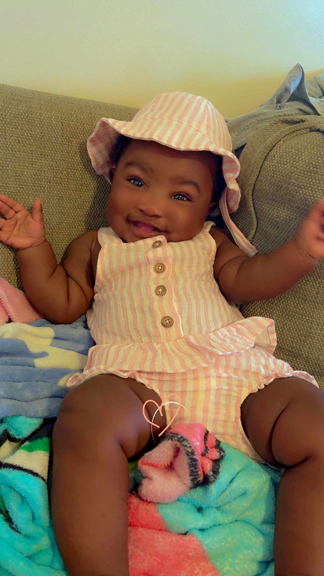 Aniya joined the competition — help win amazing prizes! baby, child, smiling, hat, striped_clothing, sitting, blanket, couch, happy, cute, indoor, person, infant, plush, relaxing, portrait, arms_up, buttoned_outfit, skin, headwear