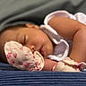 baby, infant, sleeping, peaceful, portrait, close_up, face, closed_eyes, lying_down, blanket, mittens, floral, clothing, arm, leg, cozy, indoors, soft_lighting, nap, cute