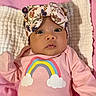 baby, infant, child, portrait, lying_down, pink_blanket, floral_headband, bow, rainbow, pink_clothing, onesie, wide_eyes, face, indoors, soft_blanket, nursery, close_up, adorable, colorful, sleeping_area