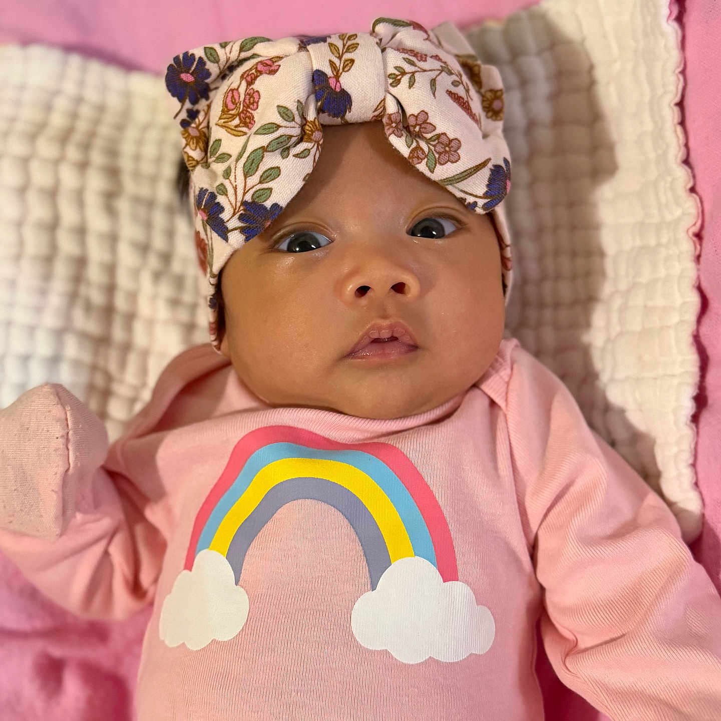 Samantha Lior joined the competition — help win amazing prizes! baby, infant, child, portrait, lying_down, pink_blanket, floral_headband, bow, rainbow, pink_clothing, onesie, wide_eyes, face, indoors, soft_blanket, nursery, close_up, adorable, colorful, sleeping_area