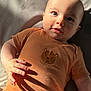 baby, brown_clothing, child, cute, expression, eyes, fabric, face, hand_shadow, indoor, infant, lying_down, onesie, person, portrait, skin, soft_texture, sunlight, tiger_graphic, wild_one_text