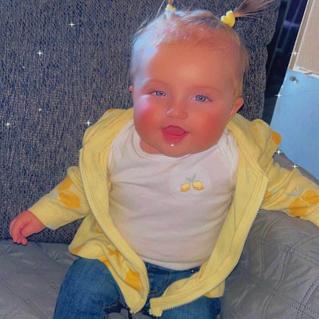 Blakely is registered to the contest to win money with this photo: baby, blonde, clothing, coat, couch, cushion, face, footwear, furniture, head, homedecor, jacket, jeans, pants, person, photography, portrait, shoe, sitting, sneaker