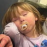 toddler, child, sleeping, pacifier, fox_design, lavender_shirt, stitch_character, hair, earrings, face, arm, cushion, indoor, resting, closed_eyes, cute, young_child, person, cozy, relaxed