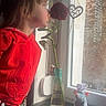 child, rose, flower, vase, window, red_hoodie, plush_toy, mouse_toy, curiosity, natural_light, indoor, plant_stem, decor, face, person, young_child, smelling, window_sill, brick_wall, casual_clothing