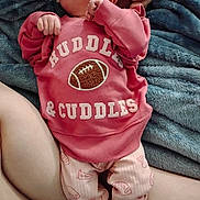 Sammie is registered to the contest to win money with this photo: newborn, baby, infant, pacifier, pink_clothing, football, onesie, blanket, adult_hand, sleeping, lying_down, portrait, close_up, home, text_on_clothing, soft_blanket, baby_pants, hands, family, cozy