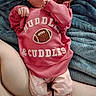 newborn, baby, infant, pacifier, pink_clothing, football, onesie, blanket, adult_hand, sleeping, lying_down, portrait, close_up, home, text_on_clothing, soft_blanket, baby_pants, hands, family, cozy