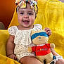 baby, child, headband, toy, plush_toy, smiling, sitting, yellow_blanket, orange_wall, cute, infant, happy, indoors, face, clothing, person, soft_toy, colorful, portrait, young_child