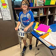 Blaine Lucas Farmer joined the competition — help win amazing prizes! boy, child, classroom, desk, educational, floor, folders, glasses, indoor, nasa_tshirt, papers, person, school_supplies, scooter, shelves, shoes, shorts, smiling, storage, wall_art