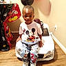 child, toddler, mickey_mouse, toy_car, balloons, birthday_party, jeans, tshirt, sneakers, indoor, wood_floor, decorations, table, chair, person, smiling, cute, celebration, play, fun