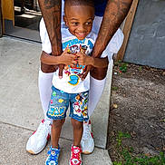 Ayan is registered to the contest to win money with this photo: child, boy, smiling, tattoos, colorful_clothing, paw_patrol, shorts, sneakers, adult, arms, outdoor, concrete, door, plants, happy, playful, holding, feet, casual, summer