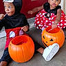 child, halloween, costume, mickey_mouse, minnie_mouse, pumpkin_bucket, lollipop, door, concrete_floor, red_background, white_shoes, cute, sitting, holiday, festive, black_clothing, red_dress, polka_dots, headwear, candy