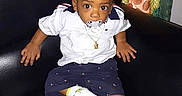 Cassius is registered to the contest to win money with this photo: toddler, child, pacifier, white_shirt, navy_shorts, white_sneakers, couch, indoor, curtains, jewelry, necklace, sitting, person, young_child, footwear, casual_clothing, home_interior, black_couch, cute, portrait