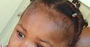 Egypt is registered to the contest to win money with this photo: toddler, child, portrait, curly_hair, hair_ties, pink_clothing, earrings, face, expression, indoor, adult_partial, black_shirt, person, young_child, closeup, cute, skin, head, looking_away, baby