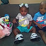Egypt is registered to the contest to win money with this photo: toddler, child, couch, nike, shirt, blue_shirt, gray_shirt, shorts, sneakers, hair_bows, plush_toy, donald_duck, toy_basket, indoor, furniture, person, sitting, curious, cute, family