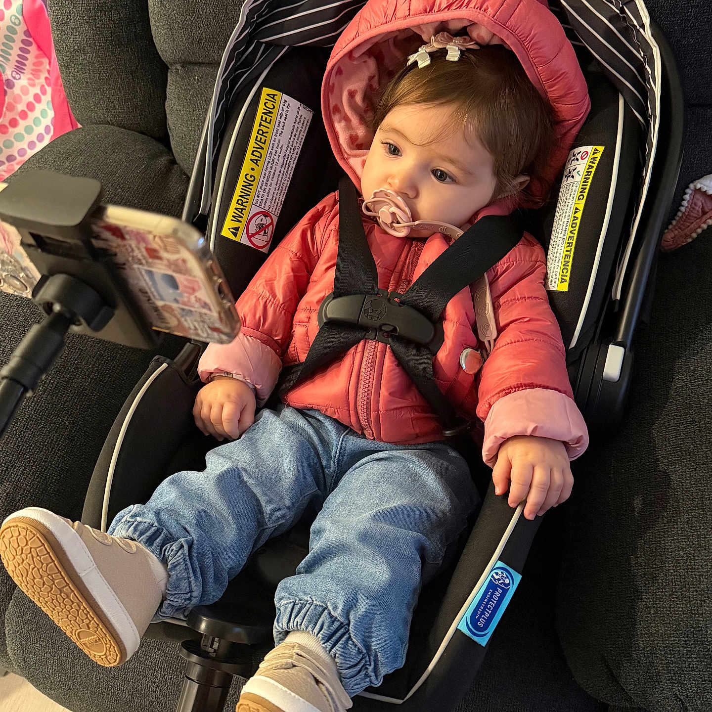 Abigail is registered to the contest to win money with this photo: baby, car_seat, jacket, jeans, pacifier, phone, indoor, child, footwear, straps, safety, cute, infant, pink, blue, person, seat, technology, couch, floor