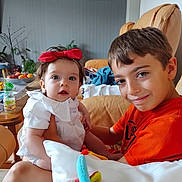 Gabriel a rejoint le concours — aidez-le/la à gagner de superbes lots ! baby, blanket, boy, child, couch, family, fruit_bowl, furniture, happy, home, indoor, orange_shirt, picture_frame, plant, portrait, red_bow, seated, smiling, table, toy