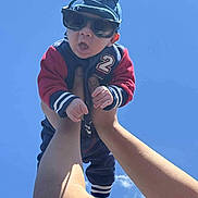 Elias is registered to the contest to win money with this photo: baby, child, sunglasses, hat, blue_sky, arms, hands, jacket, outdoor, person, cute, expression, sunny, casual_clothing, funny_face, infant, headwear, daylight, fashion, portrait